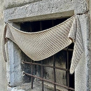 May include: A triangular knitted shawl in a light beige colour featuring a textured ribbed stitch pattern. The shawl has long, tapered ends and a wide centre section, displaying a consistent knit construction throughout the entire garment.