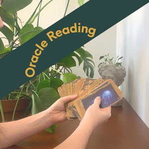 Peut inclure: Une personne tient un jeu de cartes oracle avec une image bleue et blanche. Les cartes ont des bords dorés et sont étalées. Les mots "Oracle Reading" sont affichés sur une bannière verte.