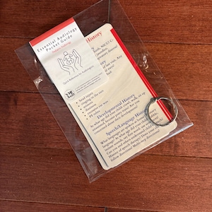 May include: A set of Essential Audiology Pocket Guide cards for paediatric audiology, enclosed in a clear plastic sleeve with a metal ring. The cards feature printed text regarding history, developmental milestones, and speech language history.