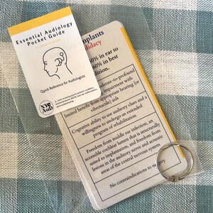 May include: A close-up of two cards with information about cochlear implants. The cards are beige with black text and are held together by a silver ring. The text on the cards includes "Essential Audiology Pocket Guide", "Cochlear Implants", "Candidacy", "50% in ear to 60% in best condition", "Limited benefit from appropriate hearing (or vibrotactile) aids", "Cognitive ability to use auditory clues and a willingness to undergo an extended programme of rehabilitation", "Freedom from middle ear infection, an accessible cochlear lumen that is structurally suited to implantation, and freedom from lesions in the auditory nerve and acoustic areas of the central nervous system", and "No contraindications to surgery".