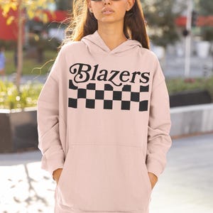 May include: A pink oversized hoodie with a black and white checkered pattern and the text "Blazers" in a retro font.