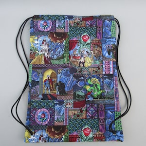 May include: Drawstring backpack with a colorful stained-glass design featuring characters and scenes from a fairy tale. The bag has a black drawstring closure and is made of fabric. The design includes images of a rose, castle, and characters.