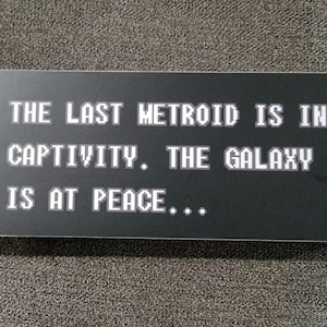 May include: Black and white text on a black background reads "THE LAST METROID IS IN CAPTIVITY. THE GALAXY IS AT PEACE..."
