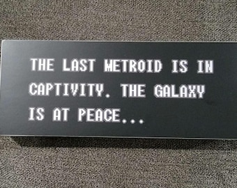 May include: Black and white text on a black background reads "THE LAST METROID IS IN CAPTIVITY. THE GALAXY IS AT PEACE..."