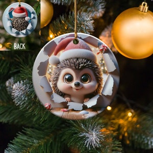 Puede incluir: Un adorno navideño redondo de cerámica con un erizo de dibujos animados que lleva un gorro de Papá Noel. El erizo asoma por un trozo de papel roto con bastones de caramelo y un suelo de madera visible en el fondo.