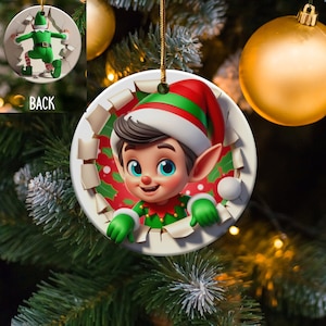 May include: A round Christmas ornament featuring a cartoon elf peeking out of a torn paper circle. The elf is wearing a green and red suit with a pointy hat and has a friendly expression.