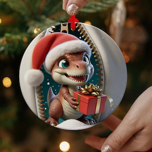 May include: A round Christmas ornament featuring a cartoon dinosaur wearing a Santa hat and holding a red gift box with a gold bow. The dinosaur is brown and green with a white belly and a toothy grin. The ornament has a white background with a blue and green zipper design.