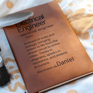 May include: A brown leather-bound notebook with the words "Electrical Engineer" and a definition printed in black. The name "Daniel" is also printed on the cover. A feather rests on the notebook.