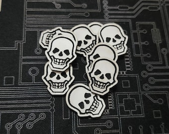 Pode incluir: Um grupo de sete adesivos de caveira brancos com contornos pretos. Os adesivos estão dispostos em semicírculo sobre um fundo preto com um padrão de placa de circuito.