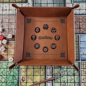 May include: A brown leather dice tray with a HeroQuest logo and monster icons. The tray is on a game board with dice.