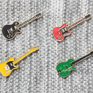 Puede incluir: Cuatro insignias de esmalte de guitarras eléctricas de diferentes colores. Las guitarras son negras, rojas, verdes y amarillas.
