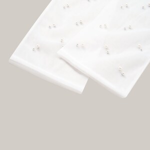 May include: A pair of white sheer gloves with pearl embellishments. The gloves are folded in half and the pearl details are visible.