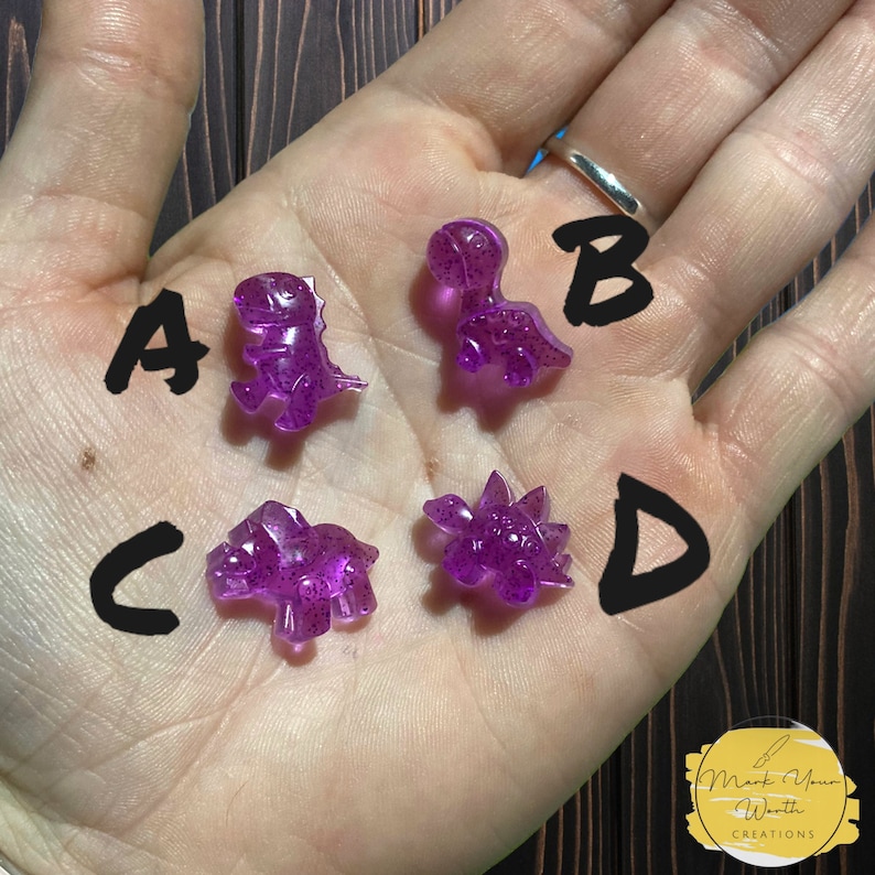 May include: Four purple glitter dinosaur figurines labelled A, B, C, and D.