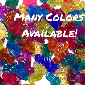 May include: A variety of colourful, glittery, plastic charms in different shapes, including stars, hearts, and animals. The text "MANY COLORS AVAILABLE!" is superimposed on the image.