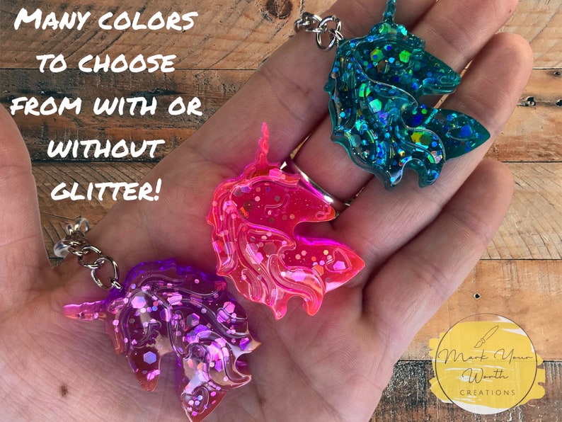 May include: Three unicorn keychains in pink, purple, and teal with glitter. The keychains are made of resin and have a silver chain.