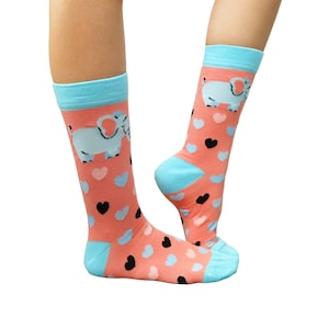 May include: A pair of pink socks with a blue elephant graphic and a pattern of pink and black hearts. The socks are shown on a model's legs.