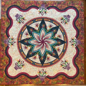 May include: A large, square quilt with a central floral design. The quilt features a cream-colored background with a large, multi-petaled flower in the center, surrounded by a circular border. The border is a mix of dark blue, red, and orange, with a scalloped edge.
