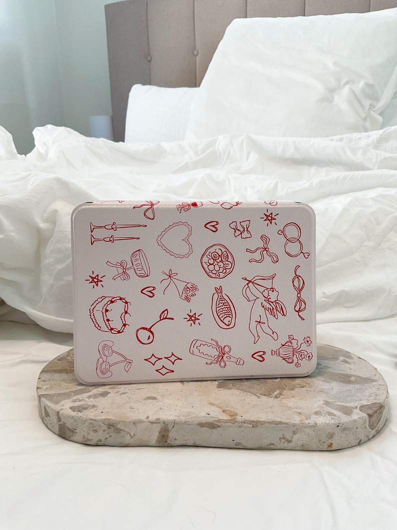 May include: White metal tin with a red and white design. The tin is decorated with various illustrations of hearts, cherries, stars, bows, and other romantic symbols.