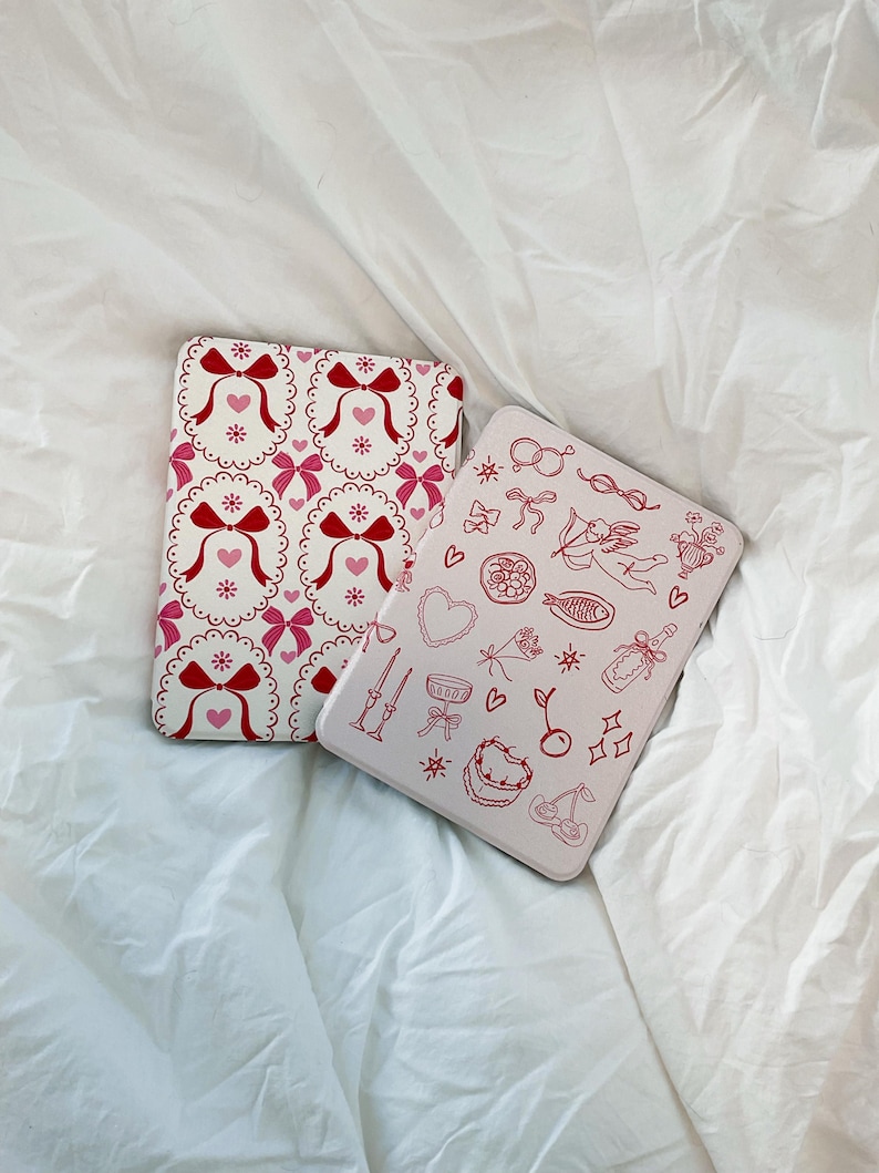 May include: Two pink and white patterned iPad cases. One case has a repeating pattern of red bows and hearts. The other case has a pink and white pattern of hearts, bows, cherries, stars, and other small details.