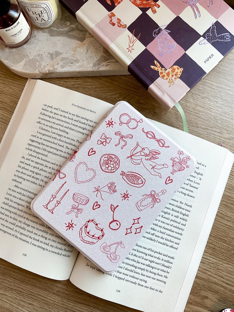 May include: A white notebook cover with a red and white design featuring cherries, stars, bows, and other small illustrations. The cover has a subtle sparkle finish.