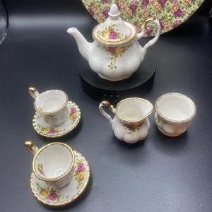 May include: A vintage tea set with a teapot, two cups and saucers, a creamer, and a sugar bowl. The set is decorated with a floral pattern and gold trim.