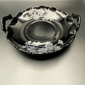 May include: A black glass serving dish with two handles and a white floral design.