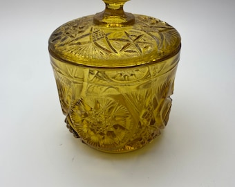 May include: A vintage amber glass jar with a lid, featuring a diamond-shaped pattern. The jar has a decorative, star-shaped design.