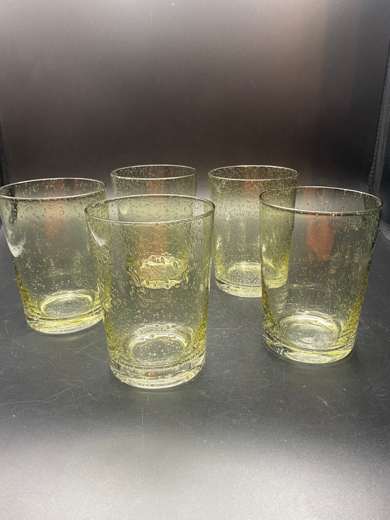 Puede incluir: Conjunto de cinco vasos transparentes de vidrio con una superficie texturizada y burbujeante. Los vasos son todos del mismo tama&ntilde;o y forma.