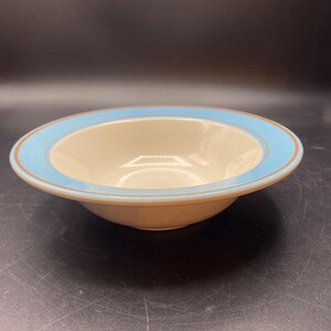 May include: A white ceramic bowl with a light blue and gold rim. The bowl is empty and sitting on a black surface.