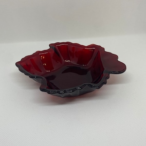 May include: A deep red glass dish shaped like a leaf. The dish has a wavy edge and is made of clear glass.