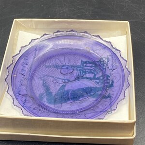 May include: A purple glass plate with a raised design of a rabbit and a carriage. The plate has a scalloped edge and the words "Mrs. Peter Rabbit" are inscribed around the edge.
