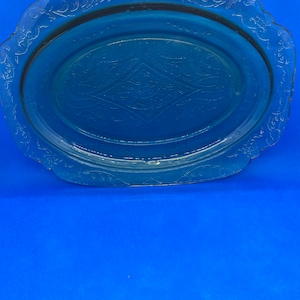 May include: A clear glass serving plate with a scalloped edge and an embossed floral design. The plate has a light green tint.
