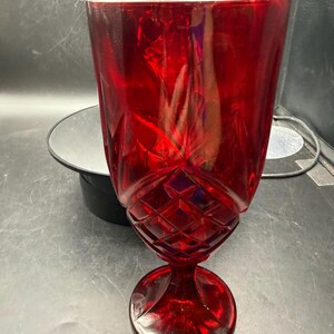 May include: A tall, vibrant red glass goblet featuring a textured diamond-cut pattern on the lower bowl and a smooth, flared rim. The stem is short and connects to a circular, stable base, with the entire piece crafted from translucent red glass.