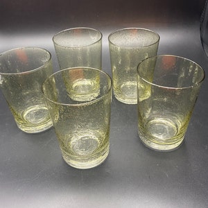 Puede incluir: Cinco vasos transparentes de vidrio con una superficie texturizada y burbujeante. Los vasos est&aacute;n dispuestos en semic&iacute;rculo sobre una superficie negra.