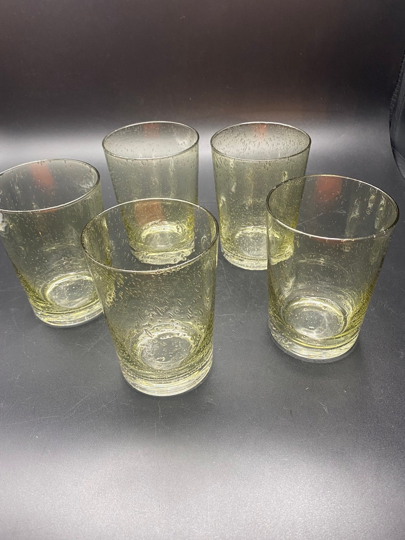 Puede incluir: Cinco vasos transparentes de vidrio con una superficie texturizada y burbujeante. Los vasos est&aacute;n dispuestos en semic&iacute;rculo sobre una superficie negra.