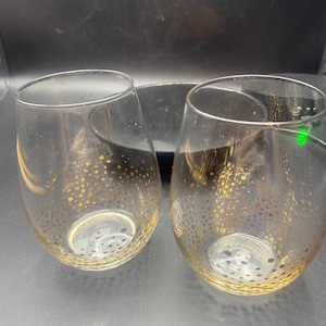 May include: Two clear glass wine glasses with a gold speckled pattern. The glasses are empty and sitting on a black surface.