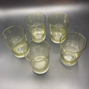 Puede incluir: Cinco vasos transparentes de vidrio con una superficie texturizada y burbujeante. Los vasos est&aacute;n vac&iacute;os y dispuestos en c&iacute;rculo sobre una superficie oscura.