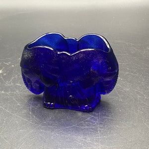 May include: A cobalt blue glass dish shaped like three elephants standing together. The dish has a textured surface.