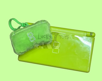 May include: A green Nintendo DS handheld gaming console with a green plush keychain featuring the Nintendo logo. The keychain has a loop for attaching to a bag or belt.