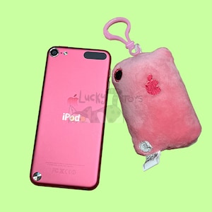 May include: A pink iPod Nano with a pink plush keychain featuring an apple logo. The keychain has a silver clip.