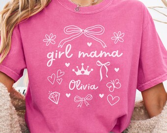 May include: Pink t-shirt with the text "girl mama" and a crown, a butterfly, hearts, and a diamond. The name "Olivia" is written below the crown.