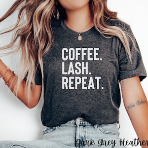 May include: A dark grey heather t-shirt with the text "COFFEE. LASH. REPEAT." printed in white.