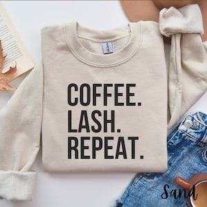 May include: A beige sweatshirt with the text "COFFEE. LASH. REPEAT." printed in black.