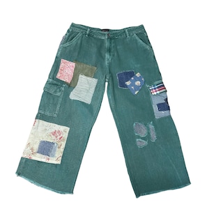 May include: Green corduroy pants with multiple fabric patches in various patterns and colors. The patches include floral, striped, and solid designs. The pants have a wide leg and cargo pockets.