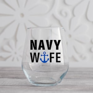 May include: A clear glass wine glass with the text "NAVY WIFE" in black lettering and a blue anchor symbol.