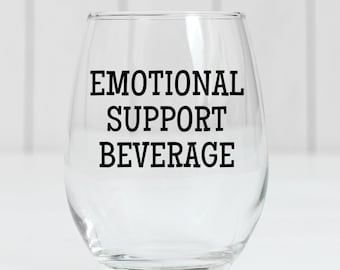May include: A clear glass wine glass with the text "Emotional Support Beverage" printed on it.