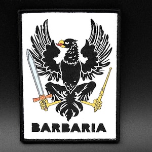 Könnte beinhalten: Gestickter Aufnäher mit einem schwarzen Adler, der ein Schwert und ein Zepter hält. Das Wort "BARBARIA" ist unten in Weiß geschrieben. Der Aufnäher hat einen schwarzen Rand. Der Adler hat einen roten Schnabel.