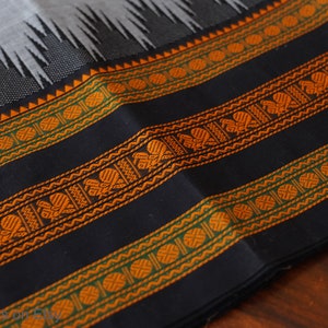 May include: Close-up of a black fabric with orange and green woven stripes. The fabric has a repeating pattern of circles and stylized flowers.