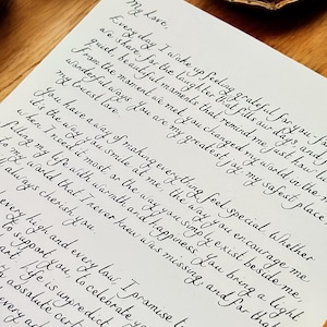 May include: A handwritten love letter with black ink on white paper. The letter expresses gratitude for the recipient's presence and love. The letter is framed and sitting on a wooden surface with a lit candle.