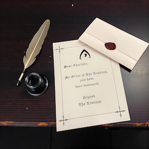May include: A vintage-style letter with the text "Dear Charlotte, By Order of The Traitors, you have been murdered." is next to a feather quill, inkwell, and sealed envelope. The letter and envelope are cream-colored.
